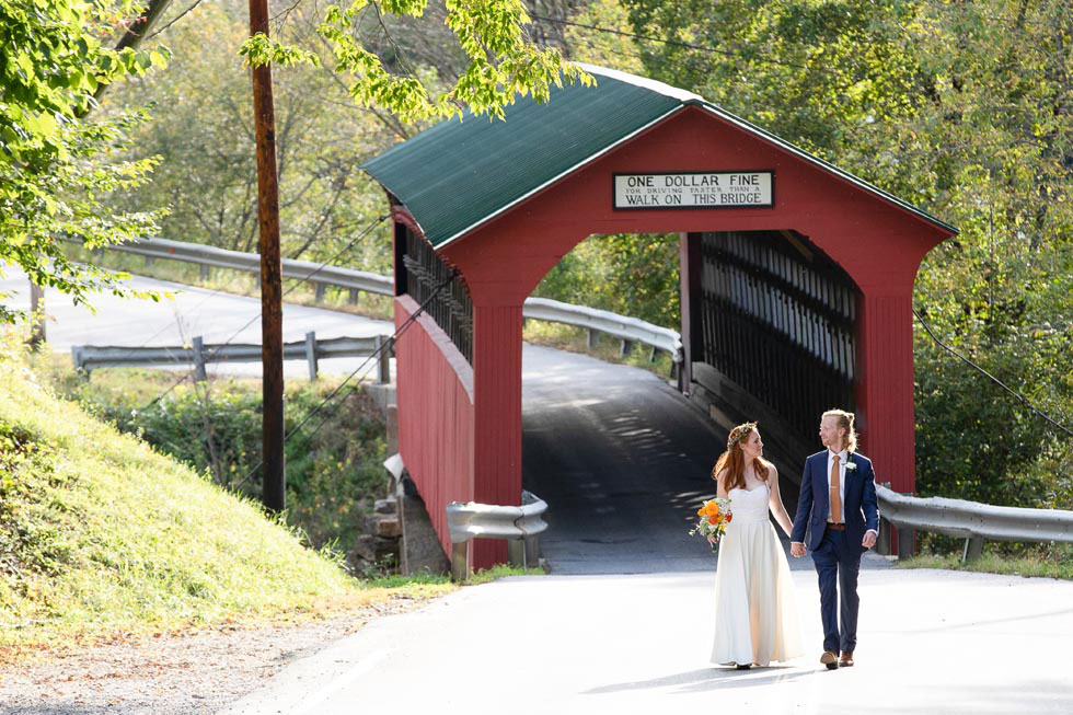 just married couple walking through covered bridge 