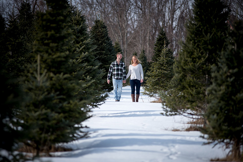 winter engagement photo couple walking christmas trees