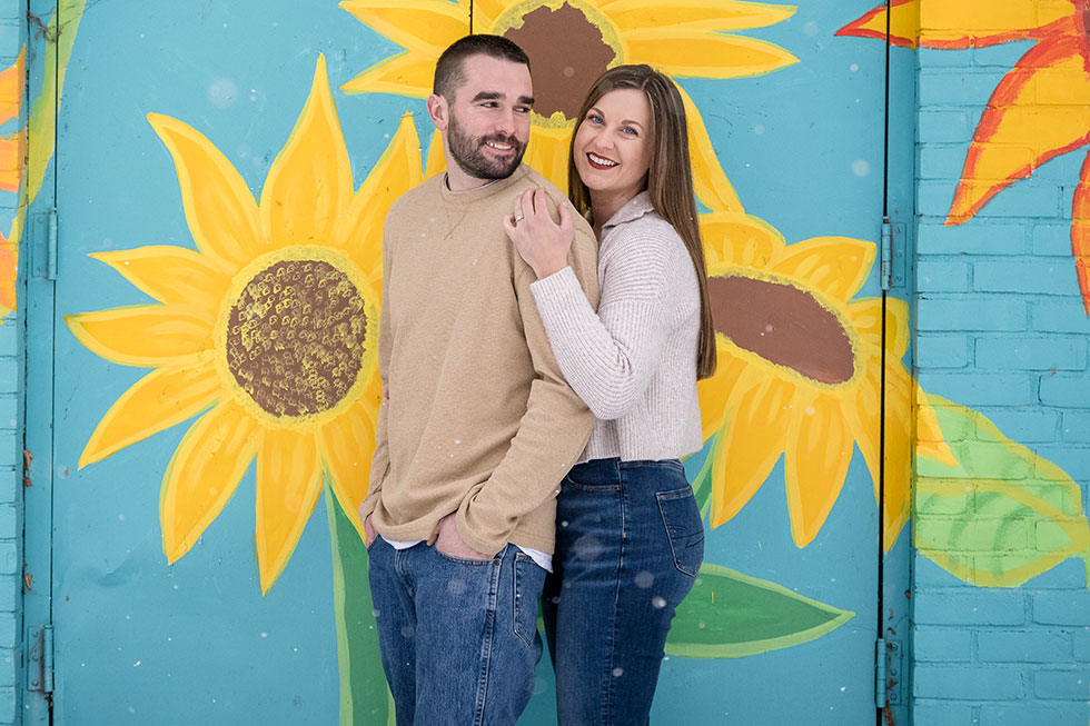 Cassie and Chad engagement photo in front of daisy mural